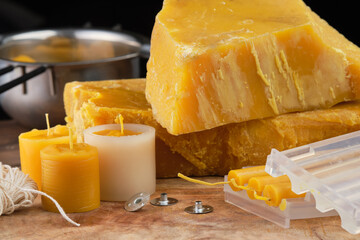 Natural beeswax blocks, a handmade candle, wick, and metal wick sustainers for crafting candles displayed on a wooden surface.