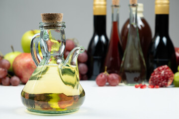 Apple cider vinegar in a vinegar cruet with spout on the background of other types of vinegars and fruits.