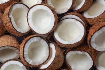 pile of coconuts cut in half in close-up view, brown fibrous husk and inner white flesh visible,...
