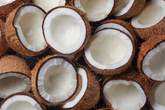 pile of coconuts cut in half in close-up view, brown fibrous husk and inner white flesh visible, abundance and freshness concept