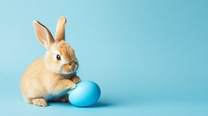 Obraz premium Easter Bunny with Egg: An adorable light brown bunny rabbit gently paws a pastel blue Easter egg against a light blue background. Perfect for Easter greetings, spring celebrations.