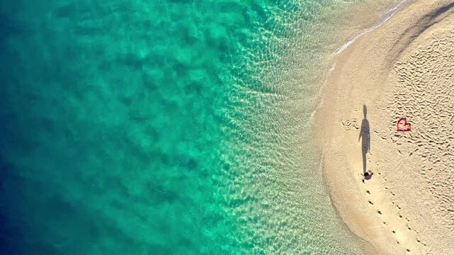 a person with long shadow in the sun is walking around the Zlatni rat beach in Croatia, aerial view