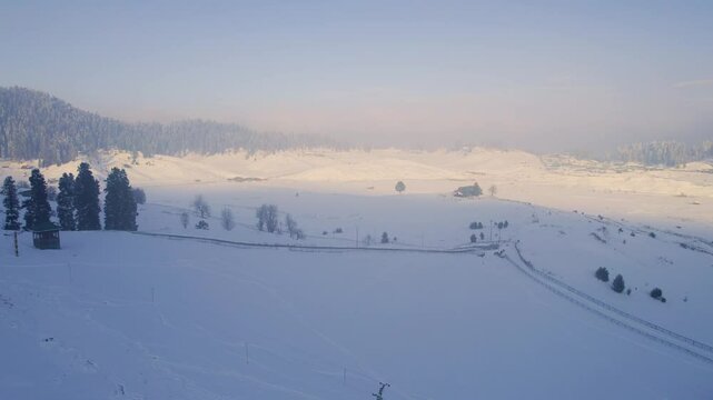 Aerial drone shot flying forward over snow covered skiing slopes in Gulmarg Kashmir with shadow and sunlight due to the himalaya mountains in paradise on earth Kashmir