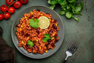 Chili con carne with minced beef, beans, paprika, corn, cilantro and red peppers in tomato sauce, tex-mex cuisine, green stone background, top view