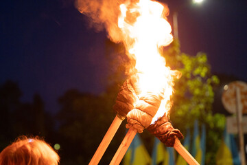 Two adults hold aloft flaming torches in the evening.  The light illuminates their faces and the...