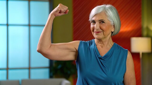 Confident Woman Flexing Arm with Silver Hair in Stylish Top, Woman flexing her arm with pride concept.