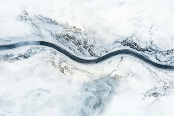 Aerial view of a winding river snaking through a snow-covered, mountainous landscape.
