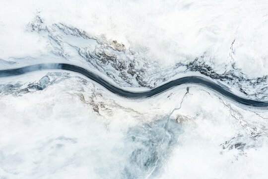 Aerial view of a winding river snaking through a snow-covered, mountainous landscape.