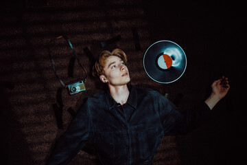 blonde young modern man lies on the floor next to a vinyl disc, looking at it lovingly while...