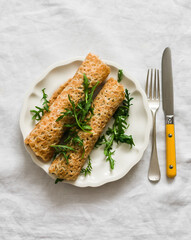 Crepes stuffed with tuna, cucumber, eggs, arugula salad on a light background, top view
