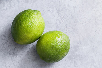 Fresh green limes on a gray concrete surface. Vibrant citrus fruit for tropical recipes. Empty copy space fruit background. Healthy drinks and organic ingredient use.