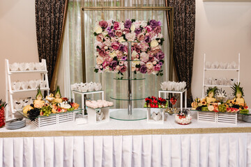 A beautifully decorated dessert table features an array of pastries, fruits, and candies. A stunning floral wall serves as a backdrop, enhancing the overall aesthetic.