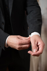 Obraz premium Close-up of a man's hands adjusting his shirt cuffs. The dark suit fabric and crisp white shirt are visible, showcasing a refined look.