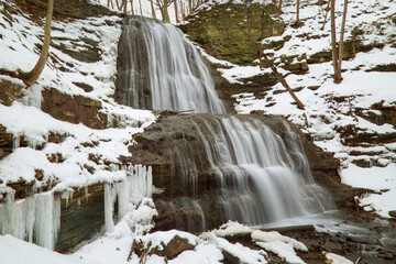 A long exposure blurred motion gorgeous cascading waterfall in the late winter, early spring, with melting snow and ice.