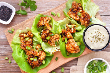 Healthy lettuce wraps with honey garlic grilled cauliflower. Above view table scene over a rustic wood background. Plant-based diet concept.