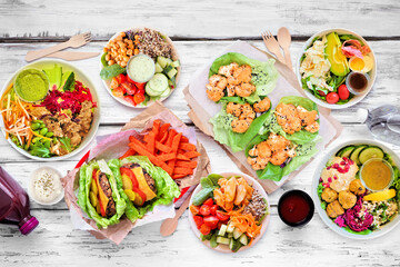 Healthy take out fast food table scene. Top view over a white wood background. Lettuce bean burgers with sweet potato fries, nutritious bowls, lettuce wraps and smoothie drink.