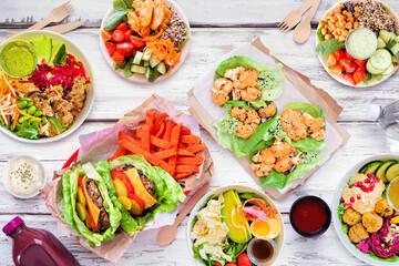 Healthy take out fast food table scene. Above view over a white wood background. Lettuce bean burgers with sweet potato fries, nutritious bowls, lettuce wraps and smoothie drink.
