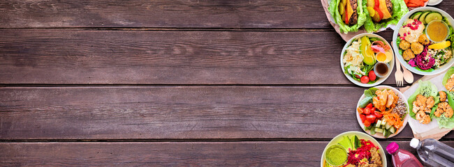 Healthy take out fast food side border. Top down view over a dark wood banner background. Table scene with lettuce bean burgers, nutritious bowls and lettuce wraps. Copy space.
