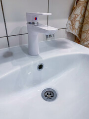 White faucet on a white sink in the bathroom, close view, white tile on the wall with black grout, towel in the distance. High quality photo