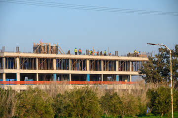 Construction workers collaborate on a new building project under a clear blue sky amidst lush greenery