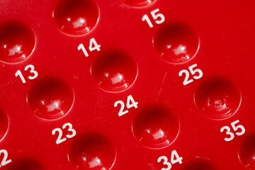 Red numbered bingo game board close-up detail, empty slots holes for bingo or lottery, random number sequence concept, row, game of chance and game theory maths abstract concept symbol, nobody