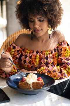 Young african woman savoring a delicious piece of cake with ice cream at a modern restaurant