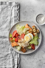 Caesar salad with chicken meat, green iceberg salad, eggs, tomatoes and parmesan cheese on gray background. Top view, flat lay