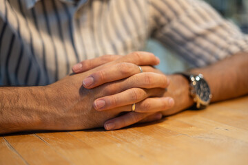 Close-up of male hands with wedding ring resting on wooden table, suggesting patience or anticipation