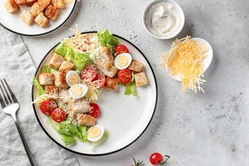 Caesar salad with fried chicken, cherry tomatoes, croutons, cheese chips, parmesan, lettuce and eggs in white plate on light background. Stylish restaurant serving, top view