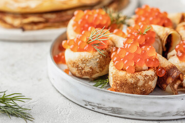 Pancake day, maslenitsa. Crepes, pancakes rolled with red caviar on white plate, close up