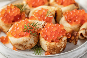 Pancake day, maslenitsa. Crepes, pancakes rolled with red caviar on white plate, close up