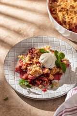 Apple crumble with ice cream on top decorated with mint leaves served in a plate on beige...
