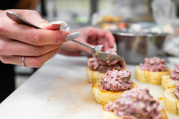 A close-up of a hand applying a savory spread onto toasted bread. The kitchen setting is visible, highlighting a culinary preparation in progress. Ideal for food-related content.
