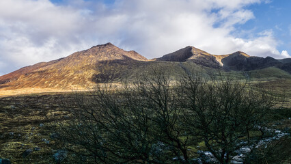 In a tranquil setting, mountains rise into the sky, illuminated by soft evening light. A stark,...