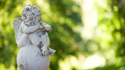 angel statue in the park. little boy with wings. cupid statue in spring park. figurine for design, marble sad angel sitting on a ball. season of love. 