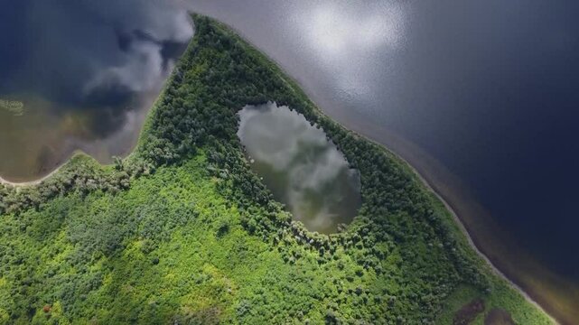 High-altitude drone view of a lush peninsula at Lake Matapedia, Quebec, Canada, featuring a hidden lake with mirror-like waters reflecting clouds amid pristine natural surroundings.
