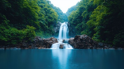 Fototapeta premium Serene waterfall cascading into a tranquil blue pool, surrounded by lush green foliage.