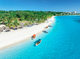 Aerial view of the boats on tropical sea coast with white sandy beach at sunset. Summer holiday in Kendwa, Zanzibar. Landscape with boat, yacht, clear blue water, green palm trees. Top drone view