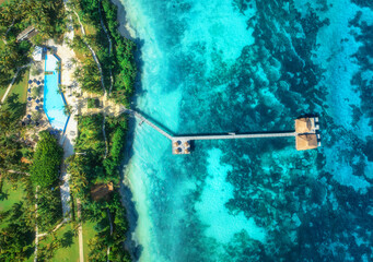 Aerial view of bungalow, jetty, white sandy beach, ocean on summer sunny day. Restaurant on the sea. Top drone view of wooden hotel, azure water, pool, green palms. Luxury resort in Zanzibar. Tropical