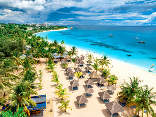 Aerial view of white sandy beach with palm trees, umbrellas, yachts, boats, blue ocean, sky with clouds at sunset. Summer holiday in Kendwa, Zanzibar island. Tropical landscape. Clear sea. Top view