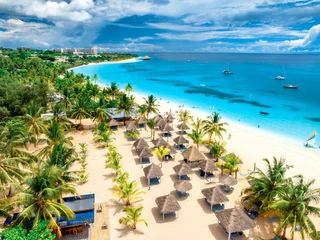 Fototapeten Aerial view of white sandy beach with palm trees, umbrellas, yachts, boats, blue ocean, sky with clouds at sunset. Summer holiday in Kendwa, Zanzibar island. Tropical landscape. Clear sea. Top view © den-belitsky