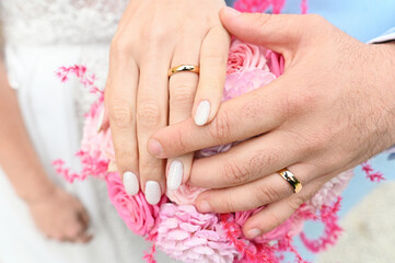 
Wedding rings on the hands of the newlyweds, a bouquet of flowers in the background. Gold rings on the hand of a man and a woman