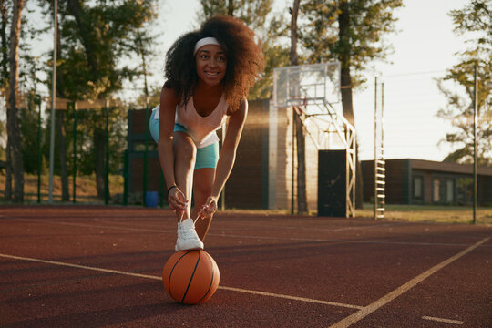 Female basketball player tying shoelaces putting foot on ball