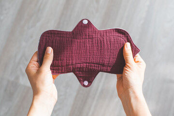 Reusable burgundy fabric muslin menstrual pad held in woman hands, sustainable and eco-friendly period product design, with neutral background, concept of ecology women's self-care during menstruation © Evgeniia Primavera
