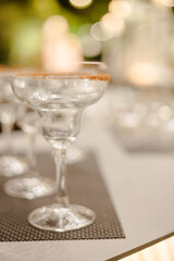 Empty margarita glasses with sugared rims sit on a table, ready for a festive event.  Soft background lighting creates a warm ambiance.