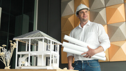 Portrait of professional project manager holding project plan with house model at table....