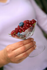 Hand holding a champagne glass filled with Raspberries, Japanese wineberries (Rubus phoenicolasius) and blueberries