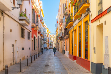 A local woman walks down narrow street of traditional whitewashed and brightly painted buildings in the downtown district of the Andalusian city of Seville, Spain.