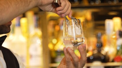 Closeup smart bartender putting ice cube with pouring soda or tonic into glass to serve customer at beverage bar counter of welcome drink with charm costume professionalism first impression. Vinosity.