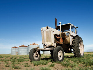 Obraz premium Old tractor in the field next to some silos, blue sky and copy space